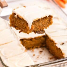 A serving of carrot cake lifted above the baking pan of carrot cake.