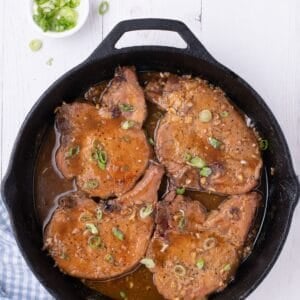Honey garlic pork chops cooked in a pan and the sauce reduced more. Garnished with optional green onions.