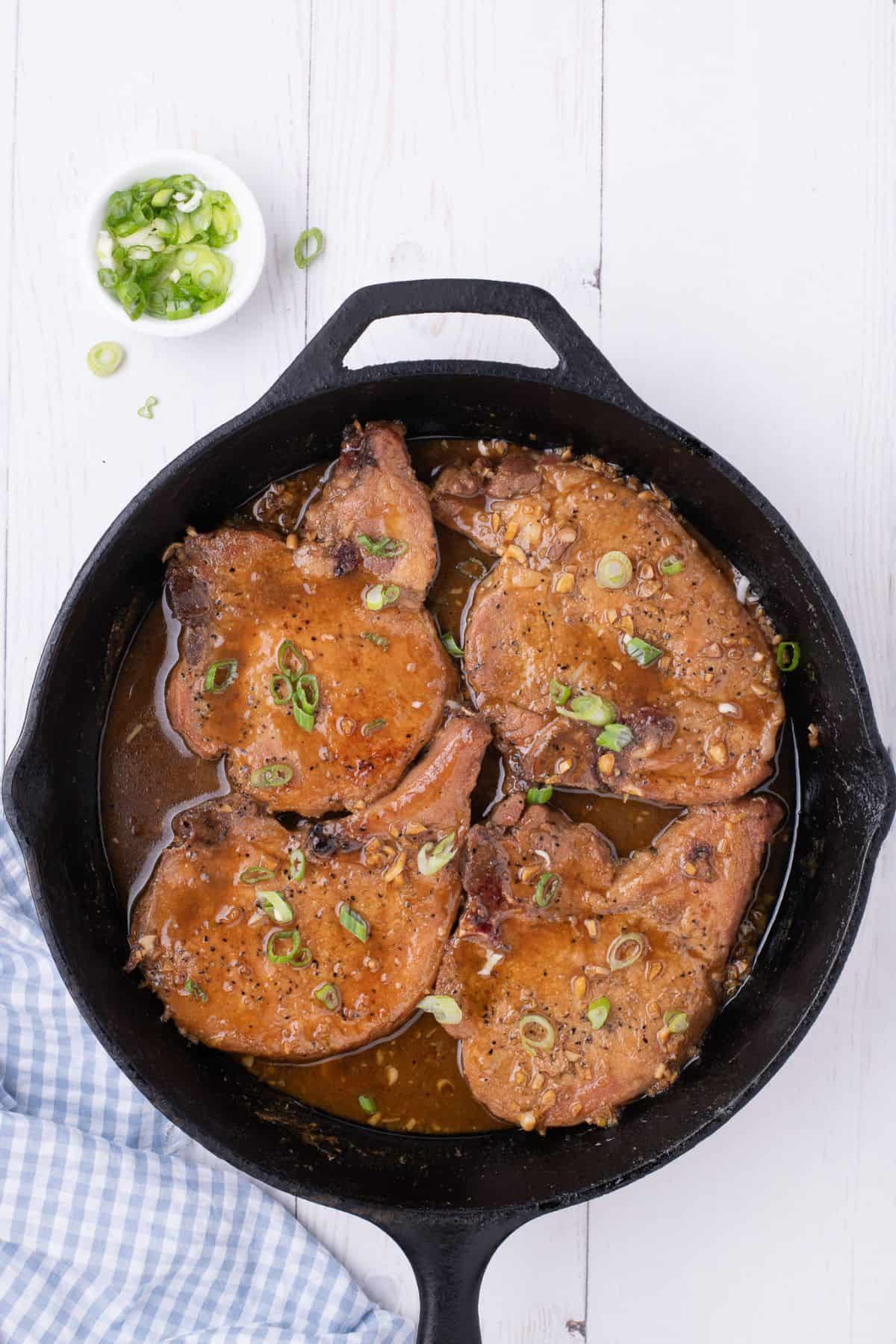 Honey garlic pork chops cooked in a pan and the sauce reduced more. Garnished with optional green onions.