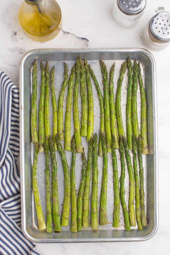 Sheet pan with roasted asparagus lined up in two rows.