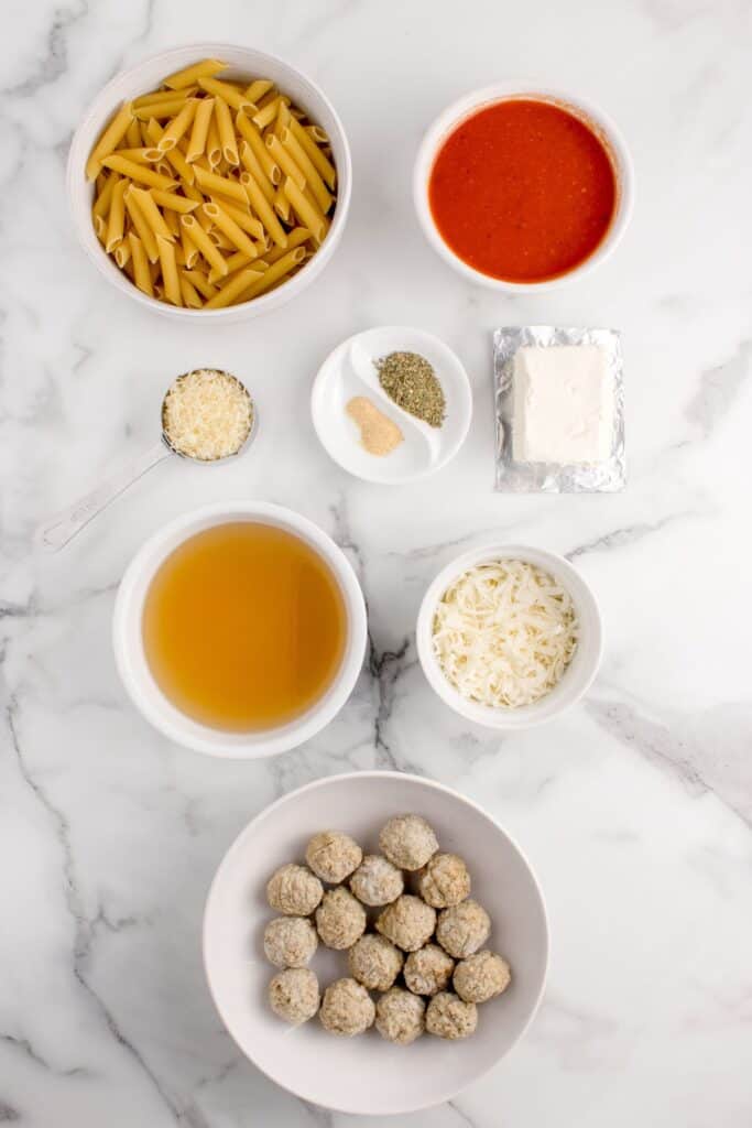 Ingredients for baked penne pasta: penne pasta noodles, pasta sauce, cream cheese, chicken broth, frozen meatballs, mozzarella cheese parmesan cheese, and seasonings.