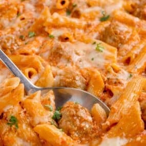 Penne pasta in a large white baking dish. A serving spoon is in the completed pasta dish.