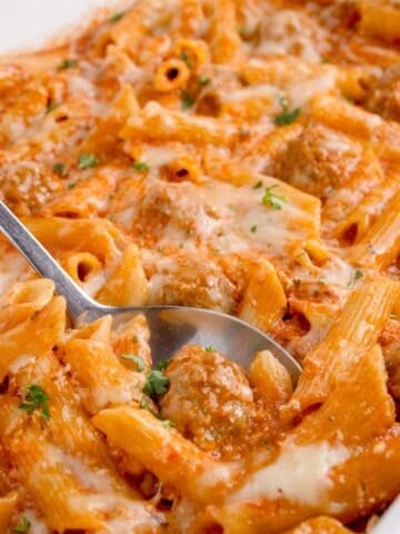 Penne pasta in a large white baking dish. A serving spoon is in the completed pasta dish.
