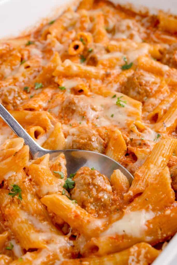 Penne pasta in a large white baking dish. A serving spoon is in the completed pasta dish.