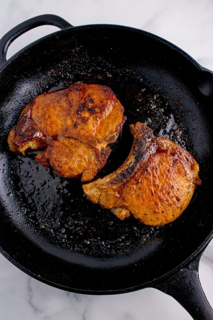 Cast iron pan with two cooked pork chops.