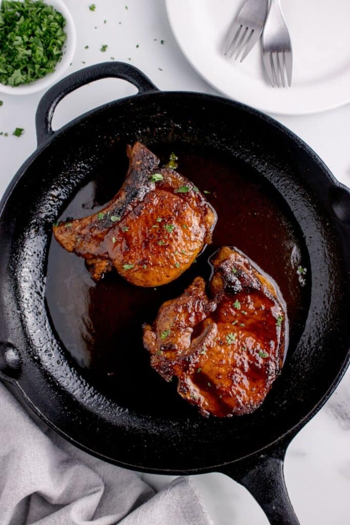 Cast iron pan with cooked pork chops and a sprinkle of parsley.