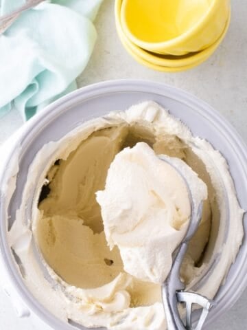 Ice cream insert bowl with homemade vanilla ice cream in it. Old fashioned scoop is lifting a serving out of the insert.