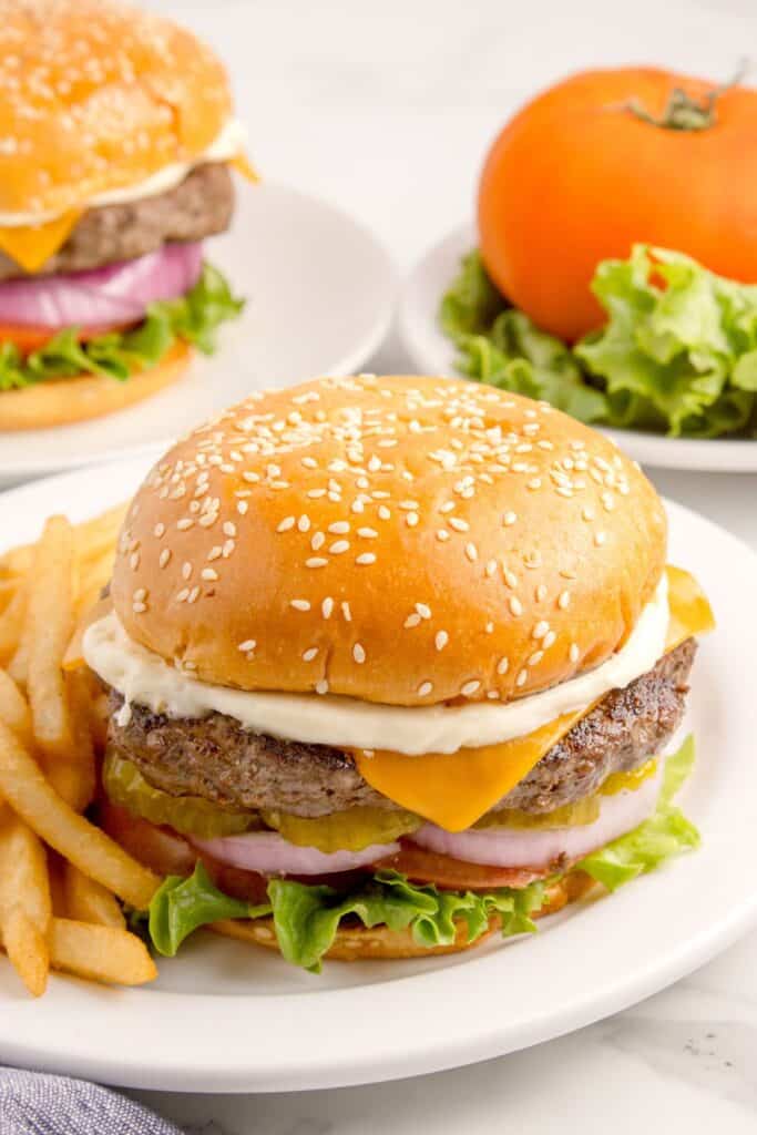 Bison burgers on white dinner plates with sides of french fries.