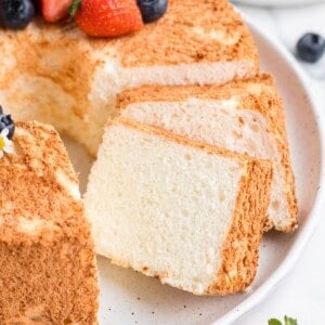 Angel food cake recipe without cake flour cut into slices with strawberries and blueberries on top.