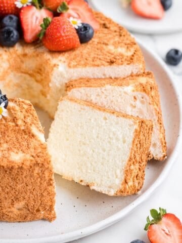 Angel food cake recipe without cake flour cut into slices with strawberries and blueberries on top.
