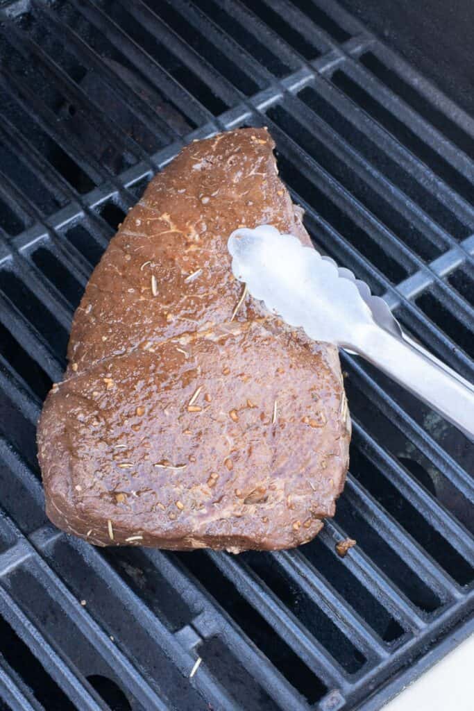 Tongs flipping roast over a grill.