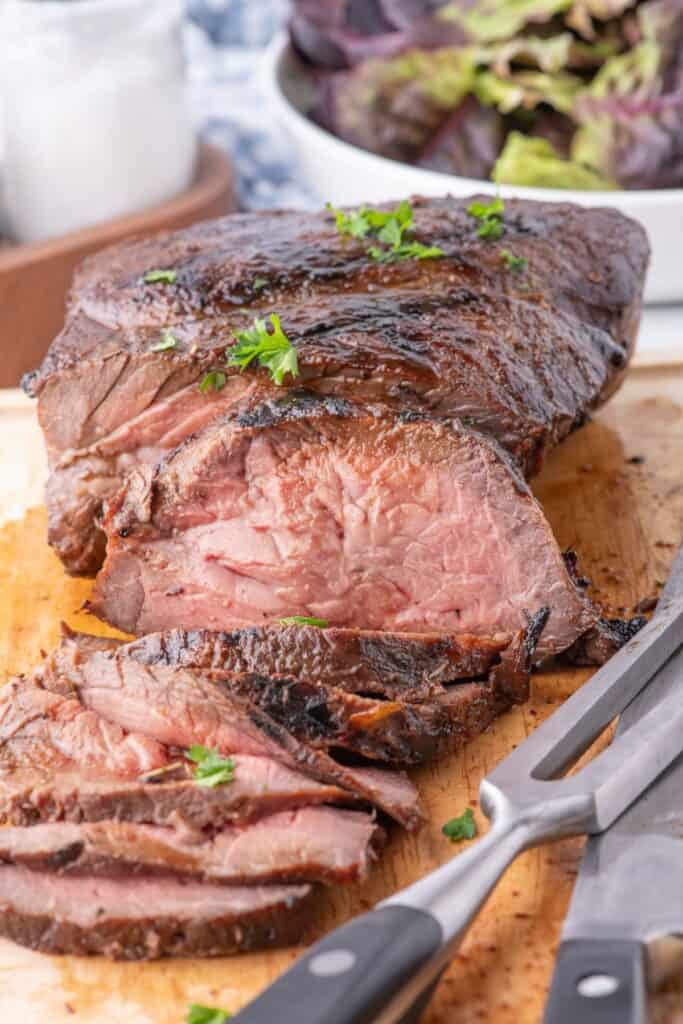 Slice London broil on a cutting board with a carving knife and fork.