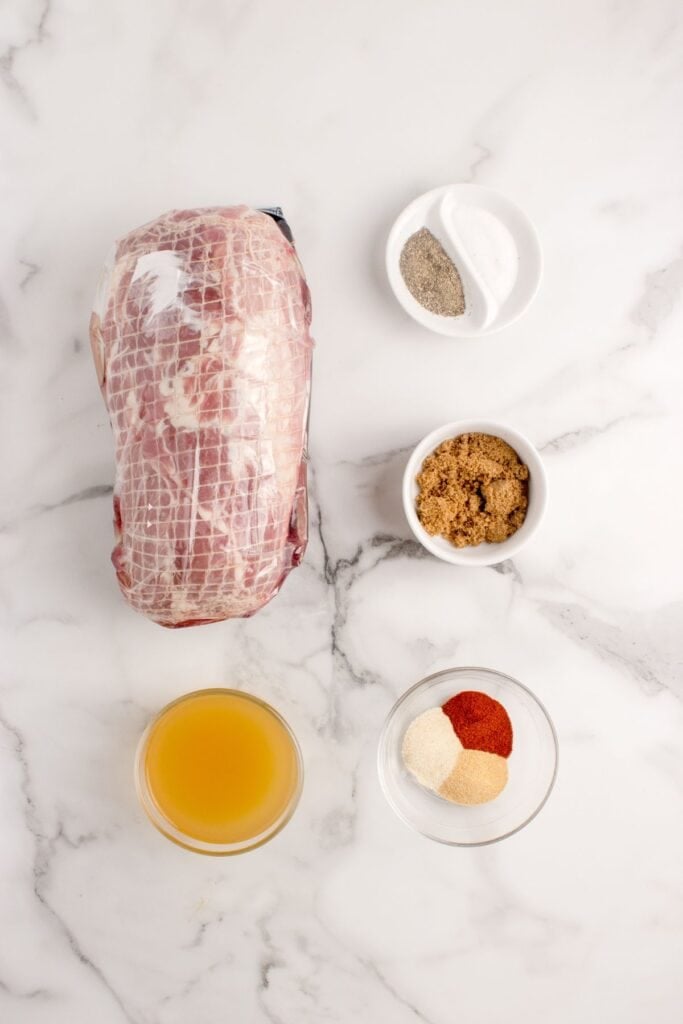 Ingredients for pork roast in a crock pot: boneless pork shoulder roast, smoked paprika, garlic powder, onion powder, salt, black pepper, brown sugar, and chicken stock.