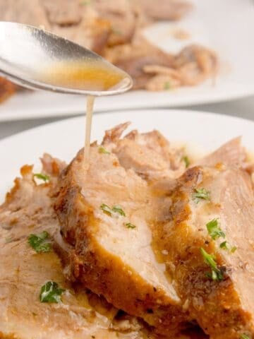 Au jus style juices being poured over the top of sliced pork roast.