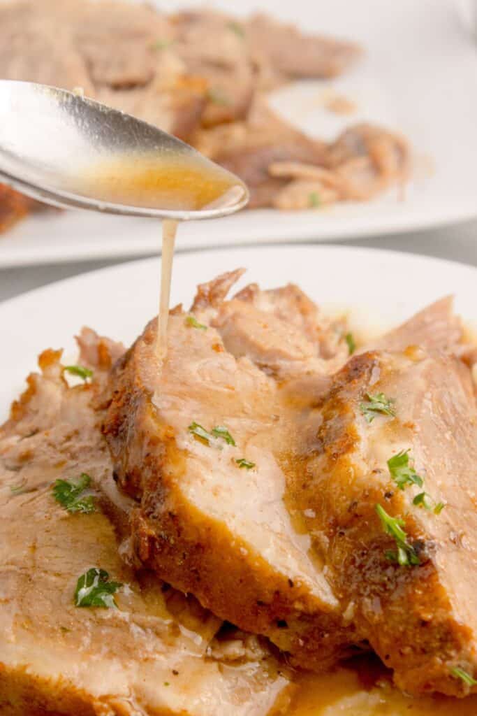 Au jus style juices being poured over the top of sliced pork roast.