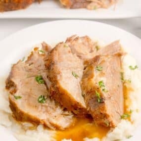White dinner plate with mashed potatoes and three slices of pork roast on top.