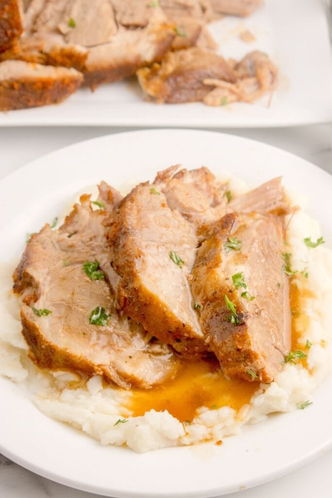 White dinner plate with mashed potatoes and three slices of pork roast on top.
