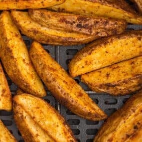 Close up of air fryer potato wedges in an air fryer basket.