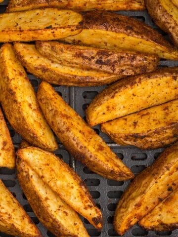 Close up of air fryer potato wedges in an air fryer basket.