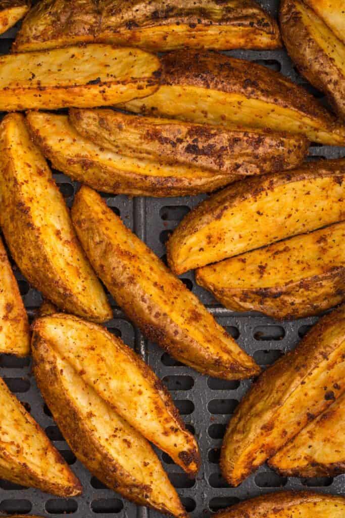 Close up of air fryer potato wedges in an air fryer basket.