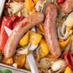 A serving spatula lifting up a serving of Italian sausage, bell peppers, and onions off a sheet pan.