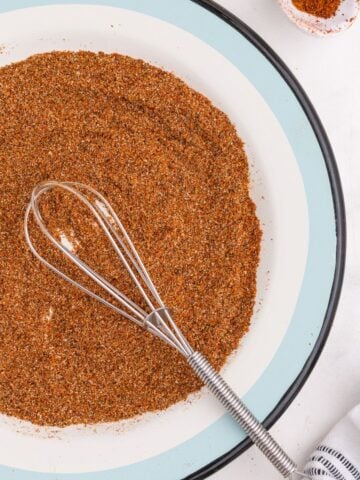 Chicken taco seasoning on a blue and white plate with a whisk.
