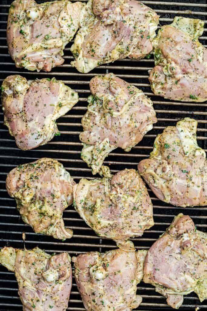 Marinated raw chicken thighs arranged on grill grates.