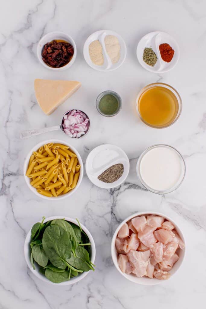 Ingredients for marry me chicken pasta: chicken breasts, penne pasta, sun-dried tomatoes, olive oil, red onions, salt, Italian seasoning, onion powder, black pepper, paprika, garlic powder, chicken broth, heavy cream, Parmesan cheese, and fresh spinach.