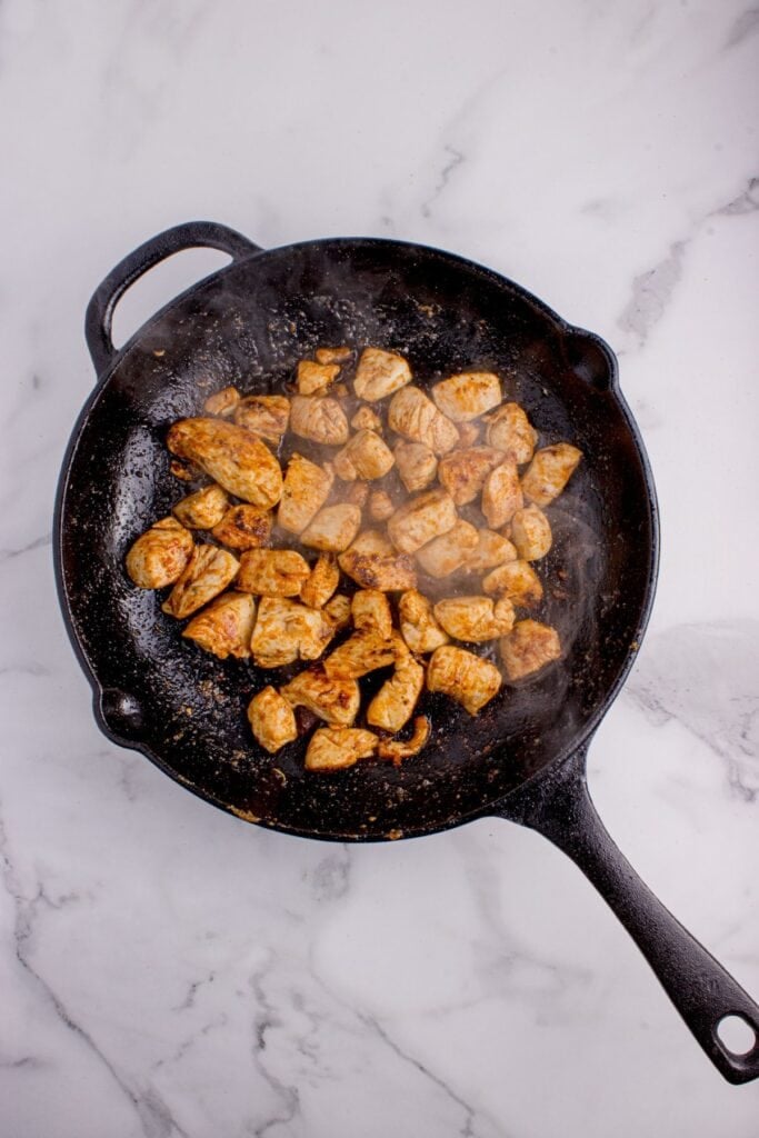 Diced chicken cooking in a cast iron pan.