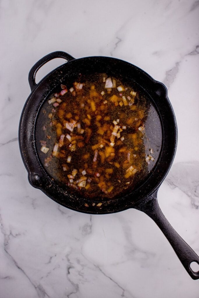 Aromatics, diced onions, and chicken broth simmering in a cast iron pan.