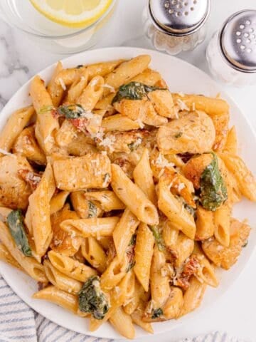 White dinner plate of penne chicken pasta.