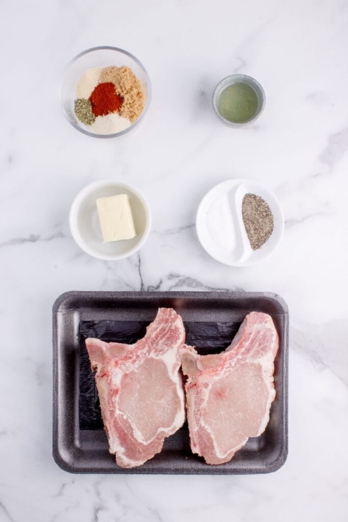 Ingredients for oven baked bone-in pork chops: center-cut pork chops, olive oil, brown sugar, garlic powder, onion powder, Italian seasoning, black pepper, smoked paprika, salt, and butter.