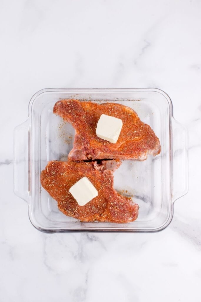 Seasoned a prepped raw pork chops in a glass baking dish with a large pat of butter on each chop.
