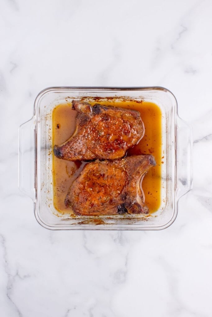 A glass baking dish with two baked pork chops in it.