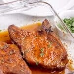 A glass baking dish with two baked pork chops with a sprinkle of parsley.