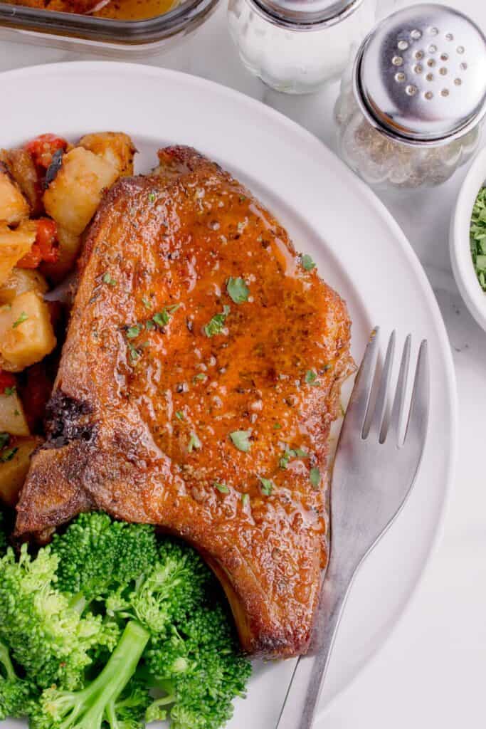 Pork chop on a white dinner plate with potatoes and broccoli.