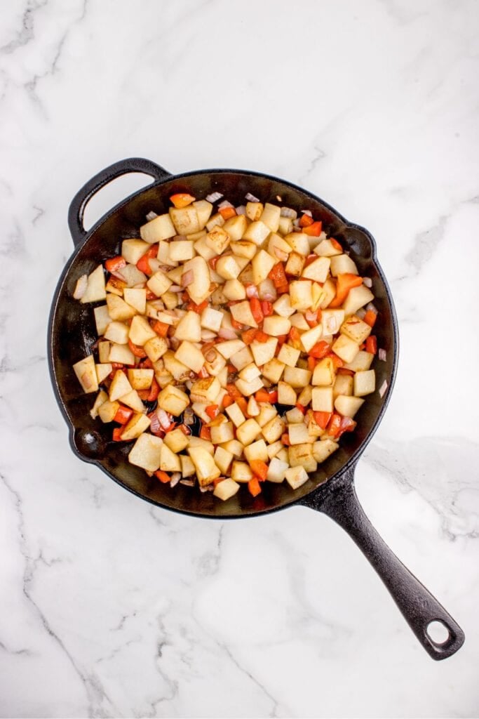 Raw, diced potatoes and bell peppers in a cast iron pan.