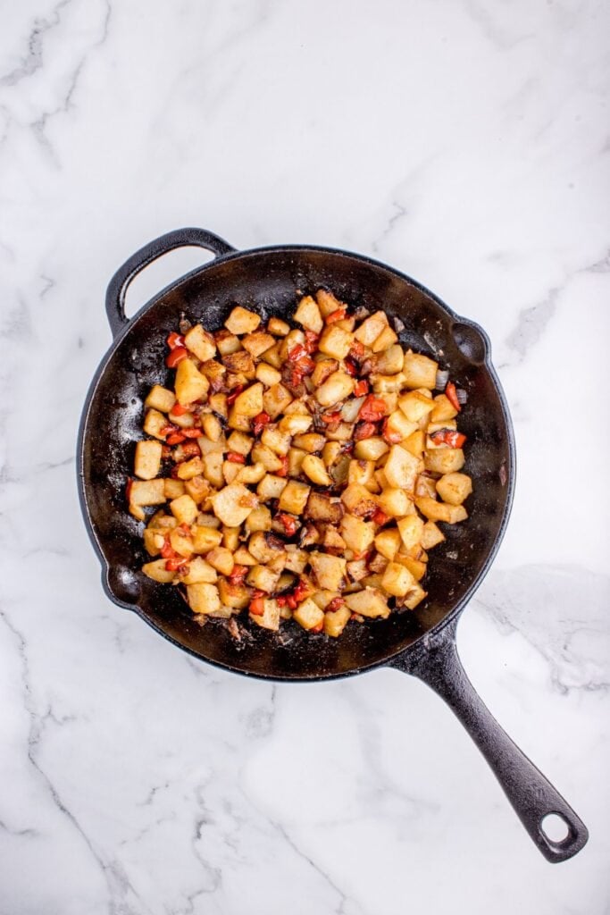 Cast iron pan with potatoes cooking in it.