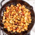 Cast iron pan with potatoes. A white dinner plate with forks and small bowl of parsley are above the pan.
