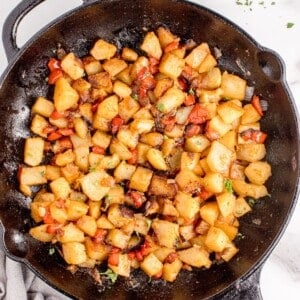 Cast iron pan with potatoes. A white dinner plate with forks and small bowl of parsley are above the pan.