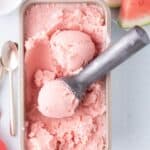 Large pan of watermelon ice cream. A scoop of ice cream is in the ice cream scoop.