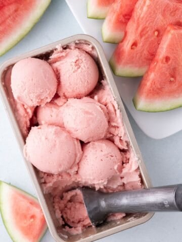 A large pan full of watermelon ice cream. The pan is surrounded by sliced watermelon.