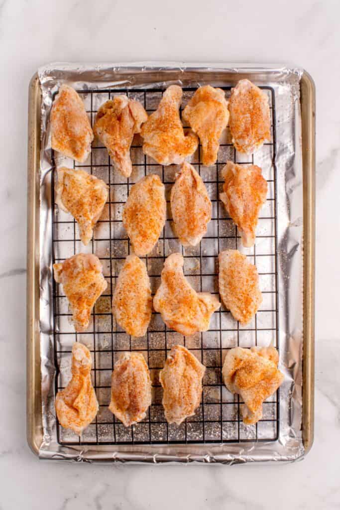 Raw and seasoned chicken wings on a wire rack over an aluminum lined baking sheet.