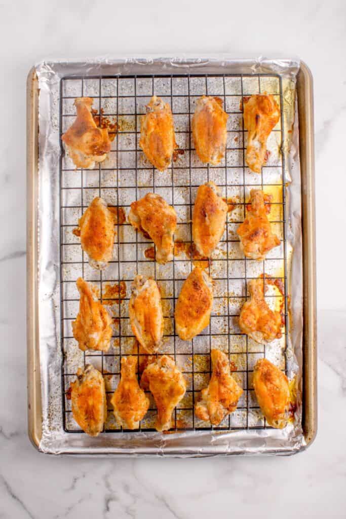 Chicken wings on a wire rack over an aluminum lined baking sheet.