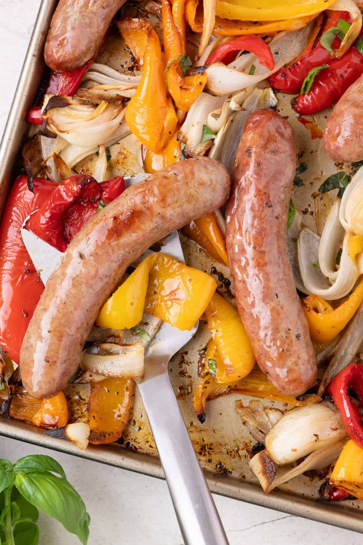Close up of the baked italian sausage with peppers and onions on a baking sheet.