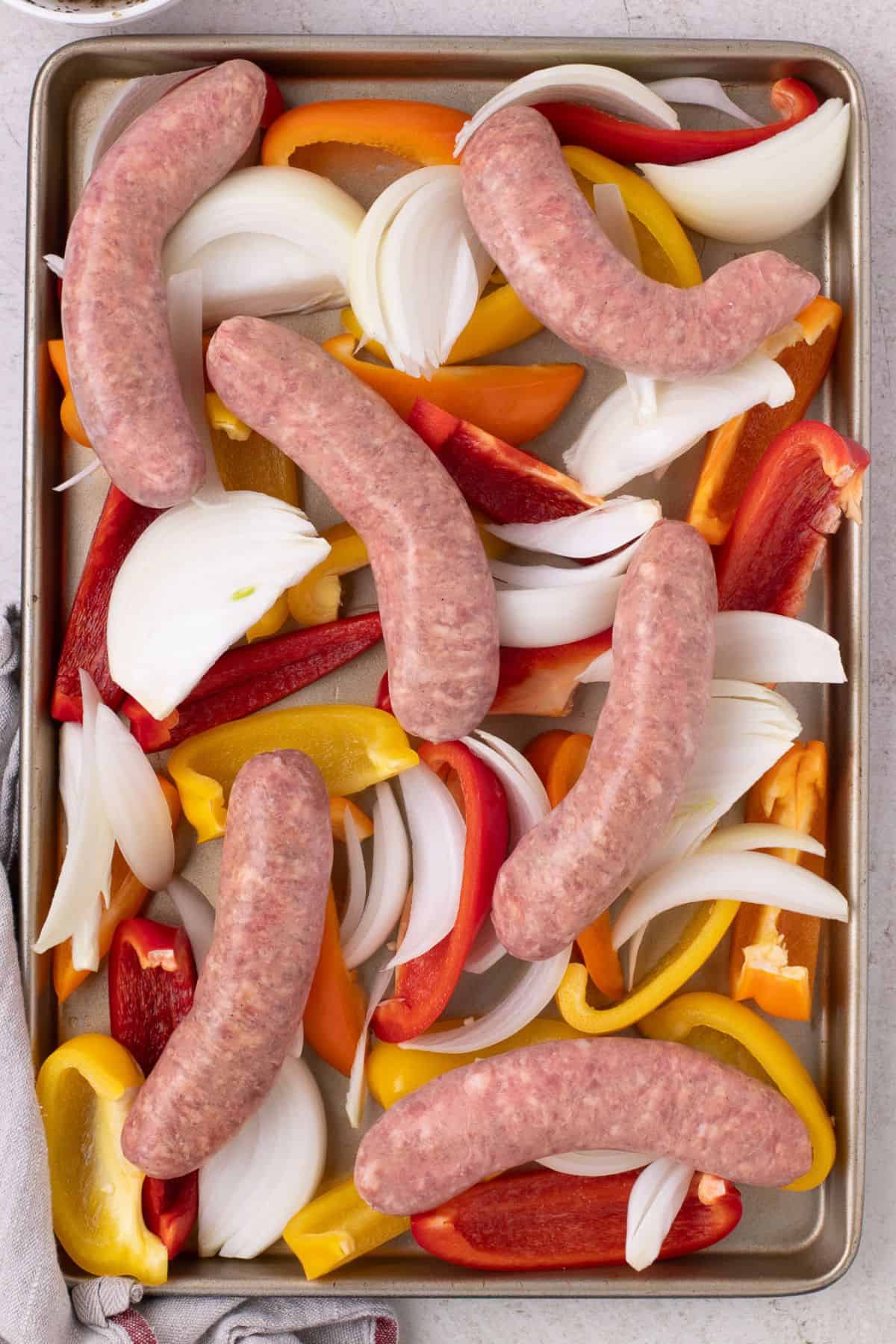 The raw Italian sausage, peppers, and onion on a baking sheet.