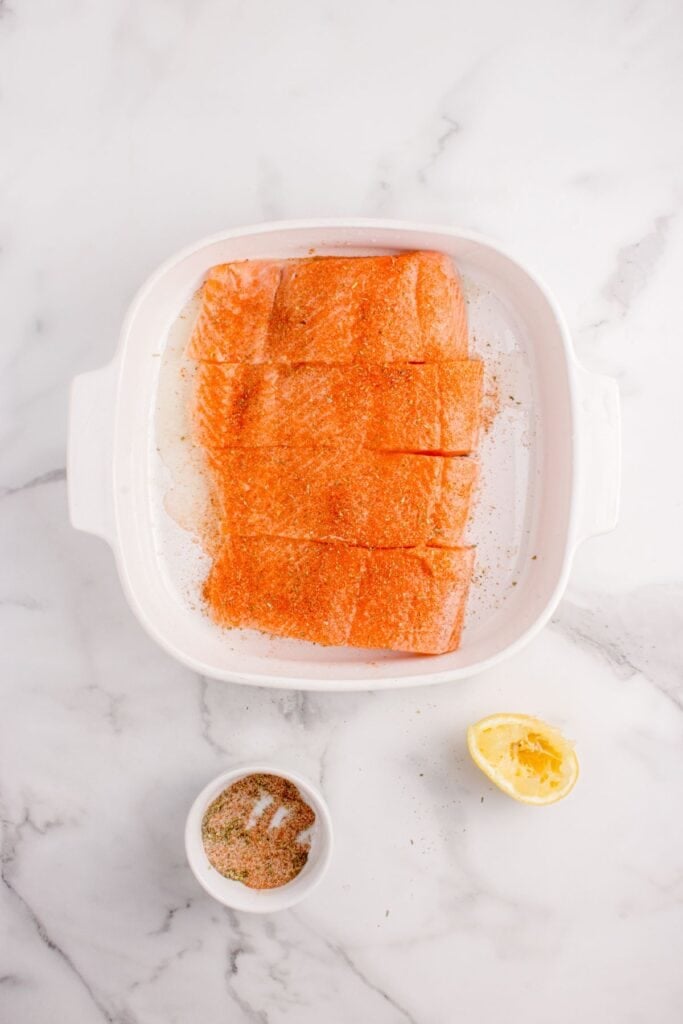 Four seasoned salmon filets lined in a baking dish.