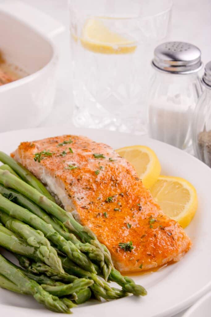 White dinner plate with asparagus and a salmon filet garnished with lemon slices.