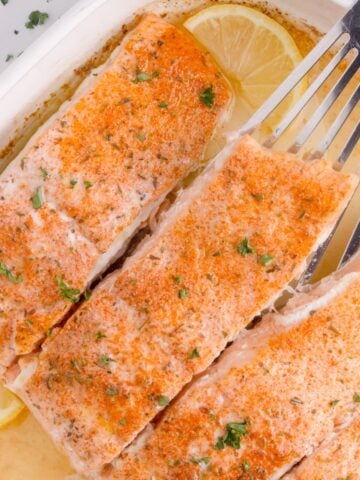 Four salmon filets in a white baking dish.