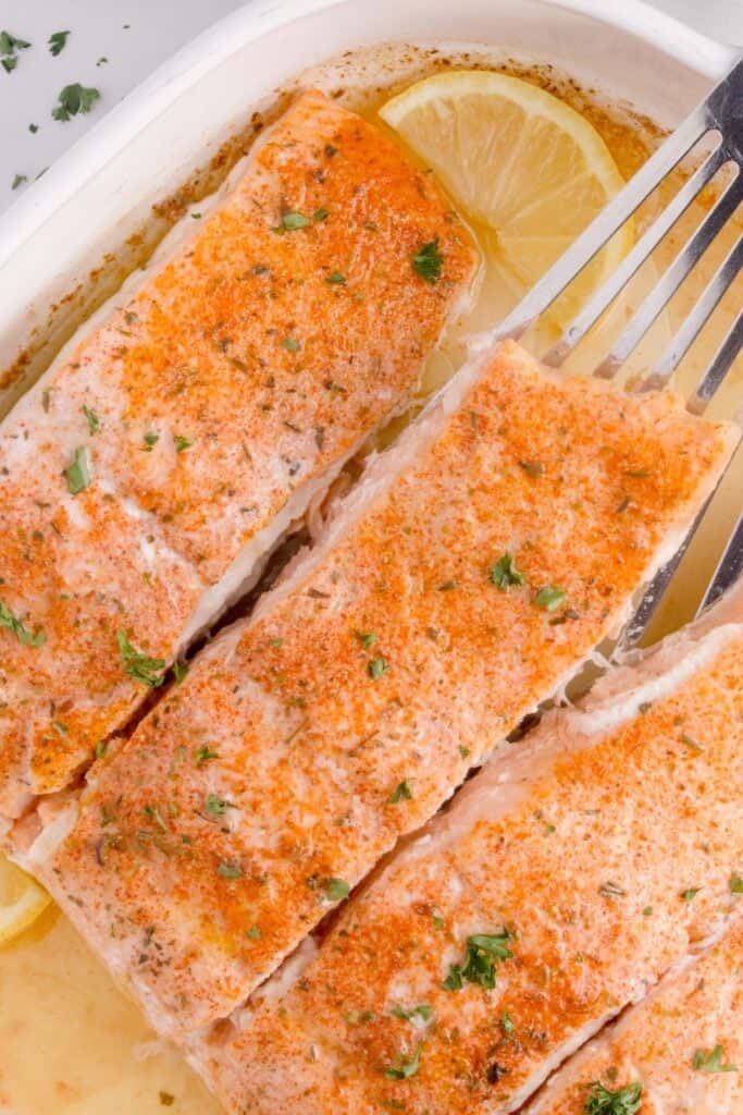 Four salmon filets in a white baking dish.